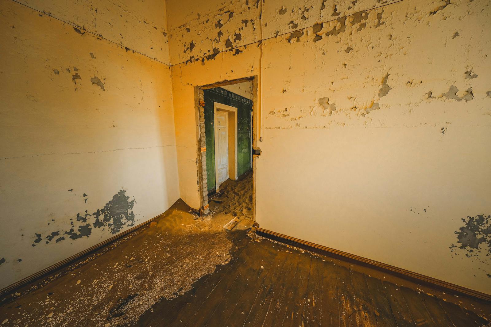An empty room with peeling paint and wood floors
