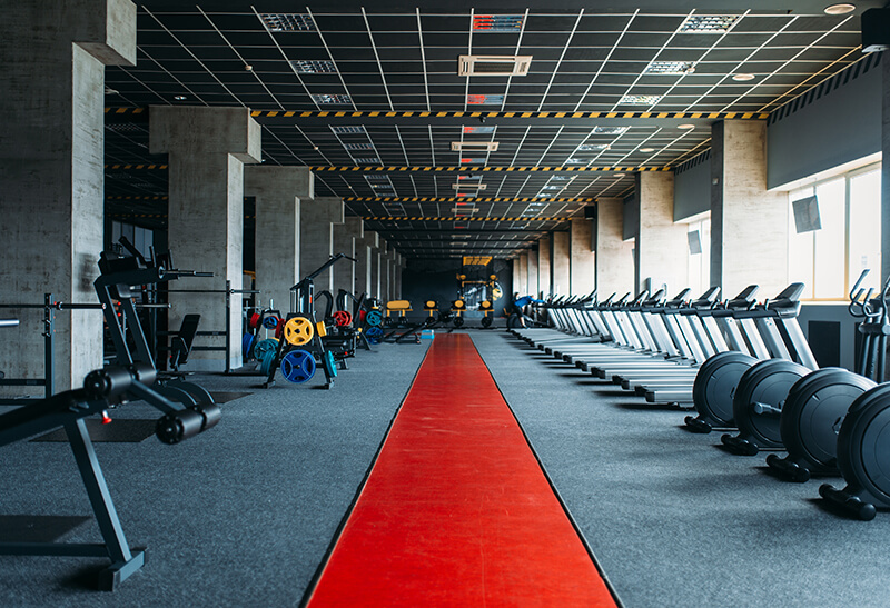 Brevard Home Cleaning - Spacious gym interior with exercise equipment, including treadmills, weight machines, and rowing machines, lined up along a red walkway—perfect for following your Gym Cleaning Checklist to maintain a spotless and safe workout environment.